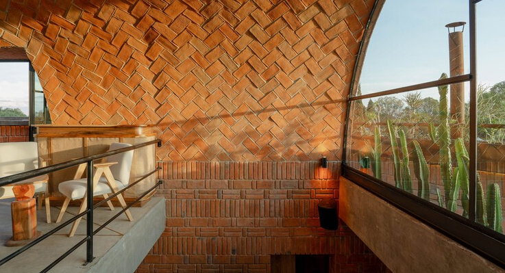 Interior de Casa Relámpago que muestra un impresiónate techo de bóveda de ladrillo en espiga, una escalera moderna con barandal de metal y un ventanal con vista a cactus exteriores, ubicado en Cholula.