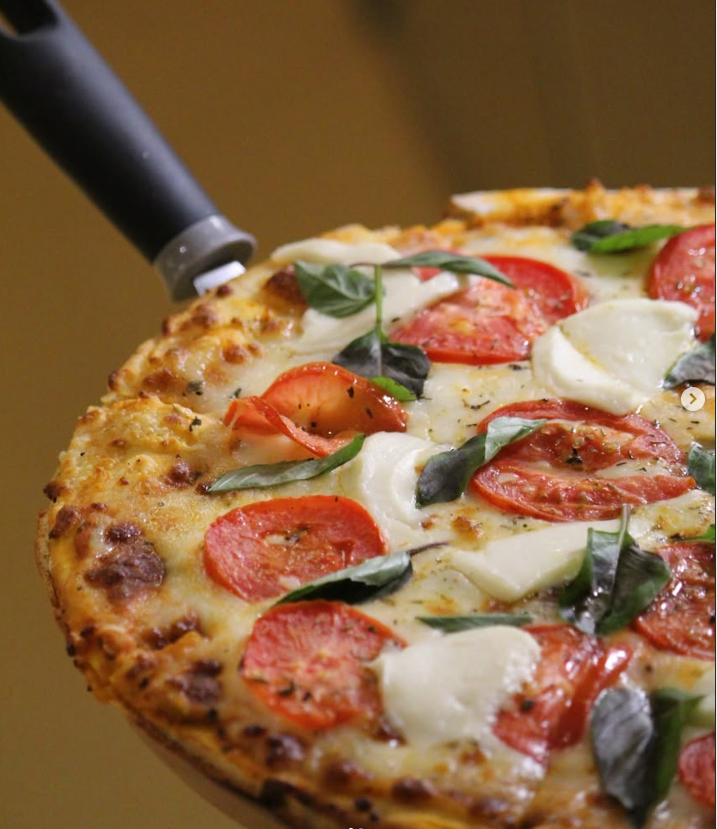 Service-3-min Pizza artesanal de Bazan Baked Goods con masa crujiente, rodajas de tomate fresco, queso mozzarella fundido y hojas de albahaca, servida en una pala de madera, ideal para el brunch.