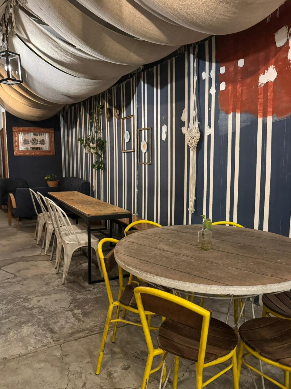 Diversión Interior de cafetería en Puebla con mesas de madera, sillas amarillas y decoración rústica con paredes rayadas, experiencia inolvidable.